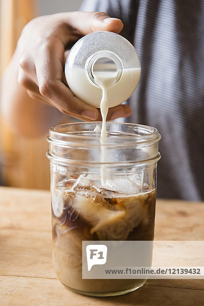 Afroamerikanische Frau gießt Milch in ein Kaffeeglas