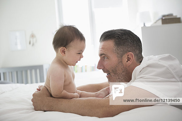 Father playing with baby son sitting on bed