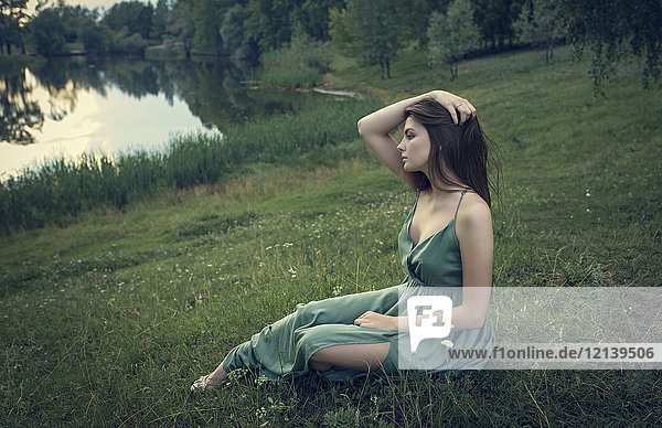 Kaukasische Frau sitzt im Gras mit Wildblumen in der Nähe eines Sees