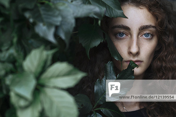 Porträt einer ernsten kaukasischen Frau hinter Blättern