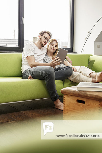Lächelndes junges Paar auf der Couch im Wohnzimmer zu Hause  das sich die Tablette teilt.