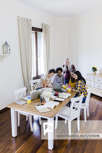 Group of female students sharing laptop at table at home