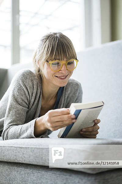 Smiling woman lying on couch reading book