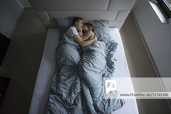 Top view of couple lying in bed at home kissing