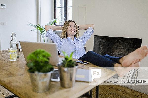 Smiling woman sitting at desk at home with feet up