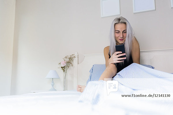 Smiling young woman in bed checking cell phone