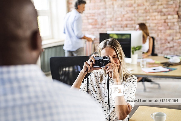 Geschäftsfrau mit Kamera beim Fotografieren eines Kollegen im Büro