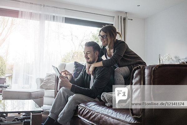 Smiling couple sittng on couch at home using tablet