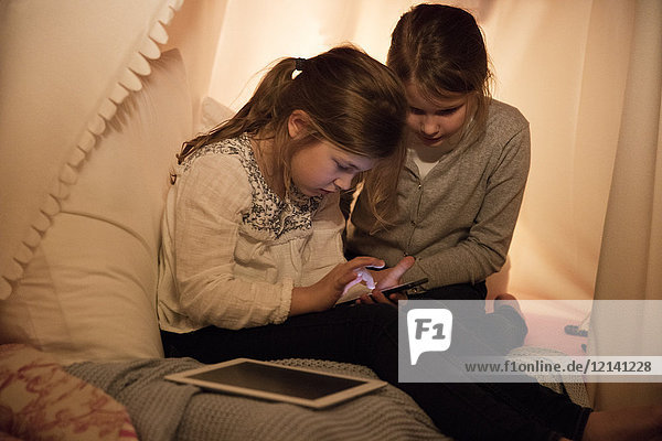 Zwei Mädchen mit Handy und Tablette im Kinderzimmer