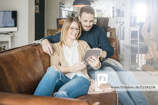 Smiling couple sitting on couch at home sharing tablet