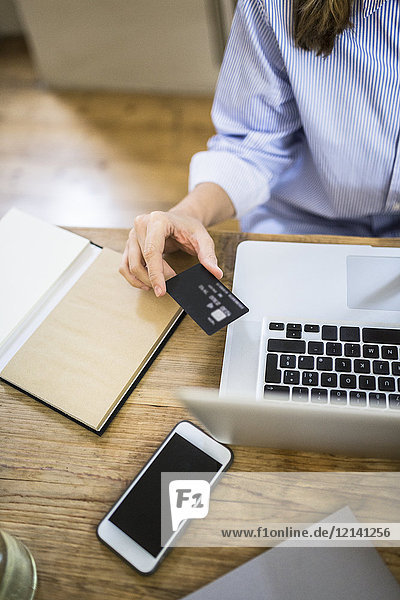 Close-up of woman at wooden desk with credit card and laptop