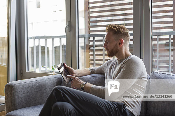 Man using mini tablet on couch in his living room