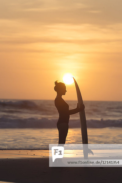 Indonesien  Bali  junge Frau mit Surfbrett bei Sonnenuntergang