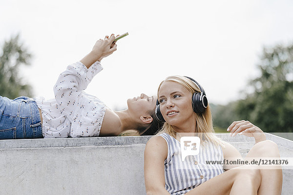 Zwei junge Frauen mit Handy und Kopfhörer im Skatepark