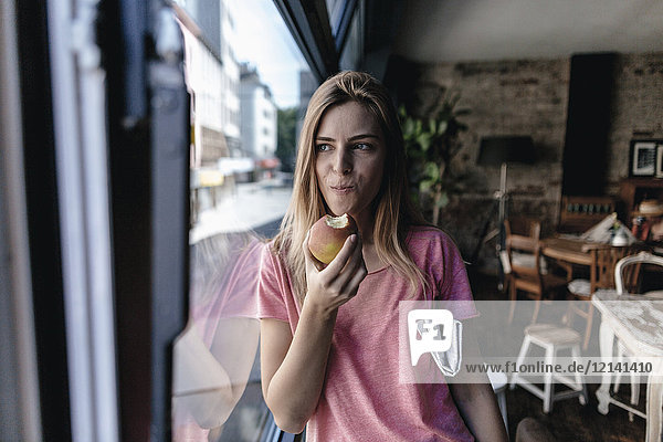 Junge Frau lehnt sich ans Fenster  isst Apfel