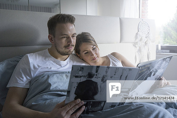 Paar im Bett zu Hause beim Betrachten des Hochzeitskatalogs