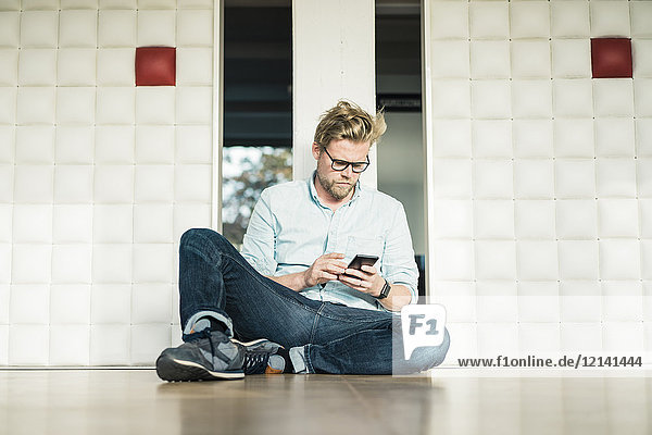Businessman in office sitting on the floor using cell phone