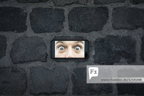 Cell phone image with eyes wide open on cobblestone pavement
