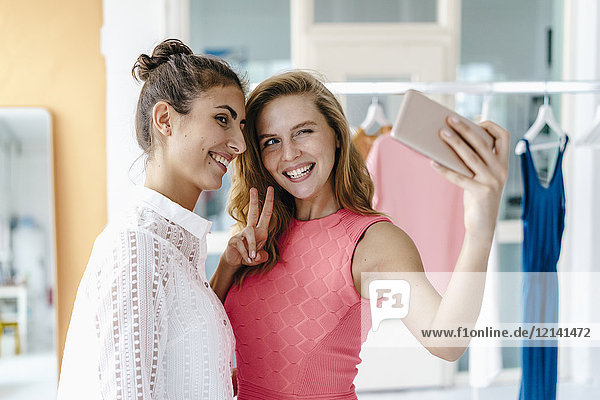 Zwei lächelnde junge Frauen  die einen Selfie im Modestudio nehmen.
