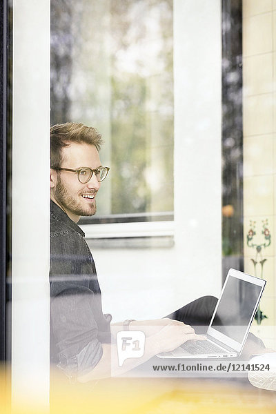 Portrait of smiling man using laptop at the window