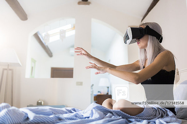 Young woman sitting in bed wearing VR glasses