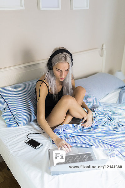 Junge Frau im Bett mit Laptop und Kopfhörer
