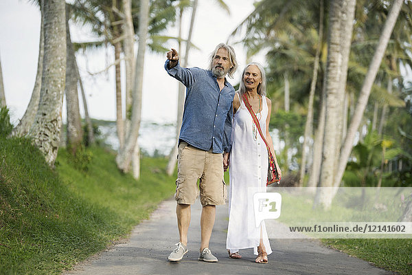 Handsome senior couple strolling through tropical landscape with palm trees
