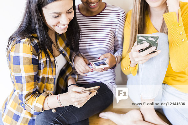 Drei glückliche junge Frauen mit Smartphones zu Hause