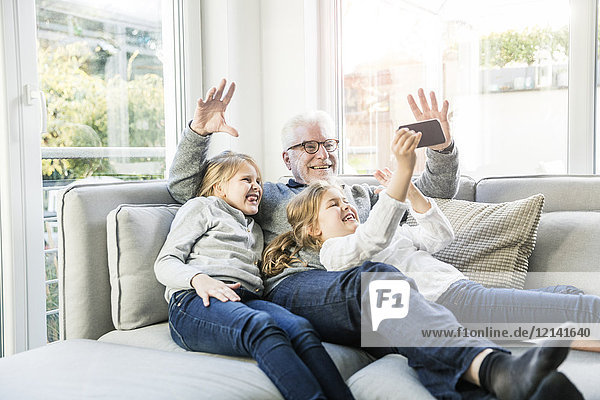 Zwei glückliche Mädchen und Großvater auf dem Sofa  die einen Selfie nehmen.