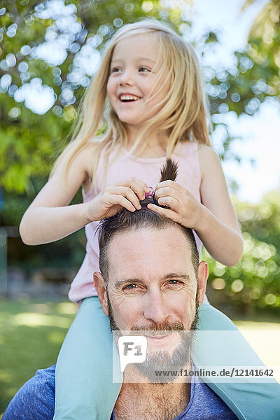 Happy girl sitting on father's shoulders doing his hair