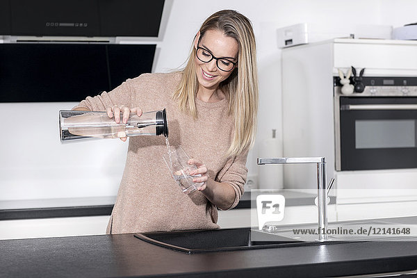 Smiling blond woman pouring water into a glass in the kitchen