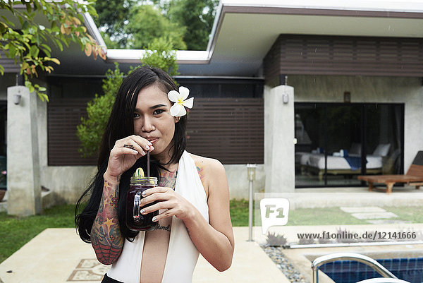 Portrait of woman with flower in her hair drinking a cocktail at a swimming pool