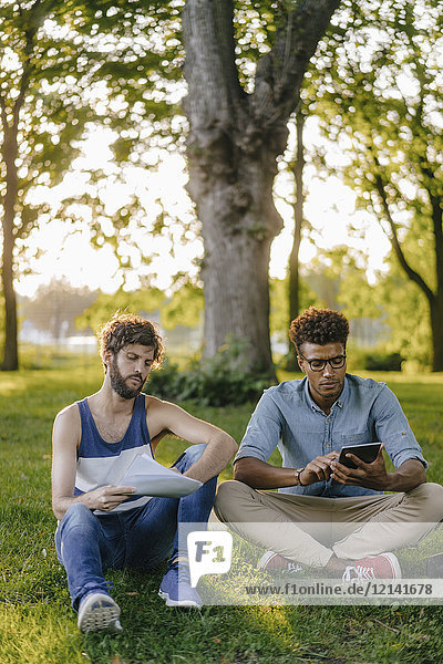 Two friends sitting in a park with mobile device and papers