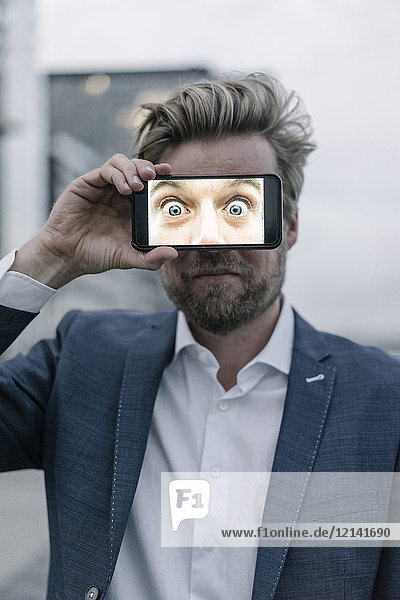 Businessman holding cell phone in front of his eyes