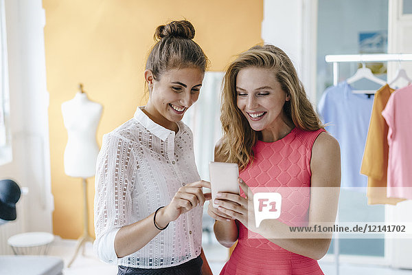Zwei lächelnde junge Frauen mit Handy im Modestudio