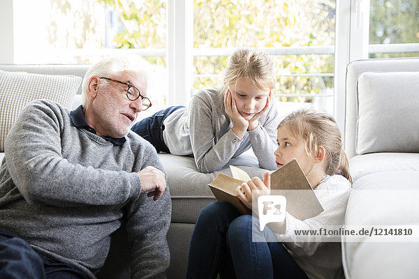 Two girls and grandfather reading book in living room