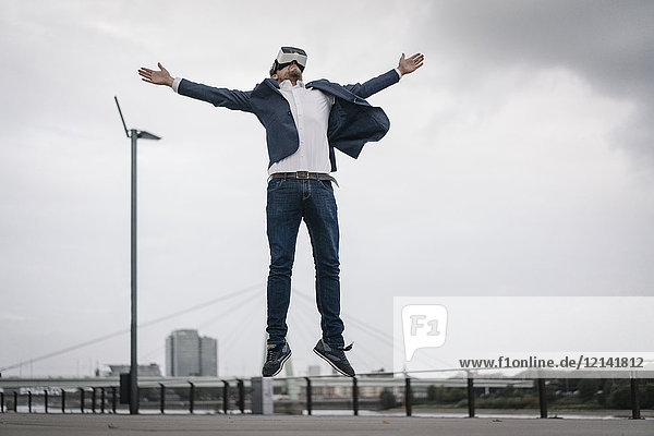 Businessman wearing VR glasses jumping in the city