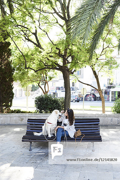 Junge Frau sitzt mit ihrem Hund auf der Bank in der Stadt