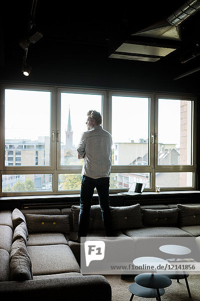 Geschäftsmann im Loungebereich eines Büros mit Blick aus dem Fenster