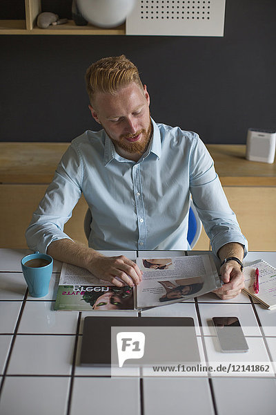 Lächelnder Mann bei Kaffee und Lesemagazin zu Hause