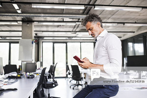 Mature businessman using cell phone in office
