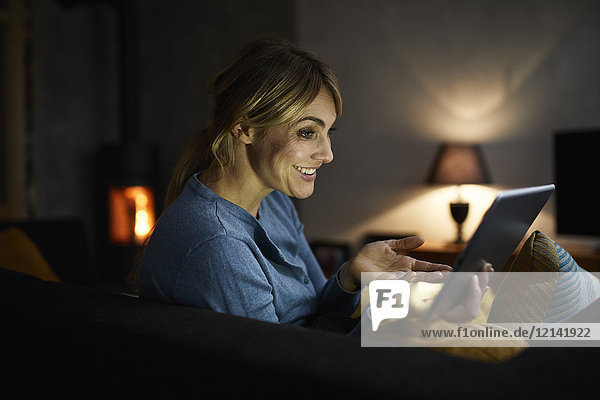 Porträt einer lächelnden Frau,  die abends zu Hause eine Tablette benutzt.