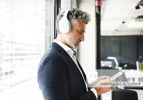 Mature businessman at the window in office with headphones and cell phone