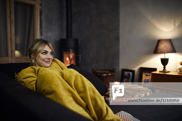 Porträt einer lächelnden Frau  die sich abends zu Hause auf der Couch ausruht