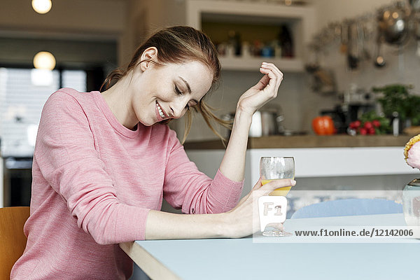 Lächelnde junge Frau mit einem Glas Orangensaft in der Küche zu Hause