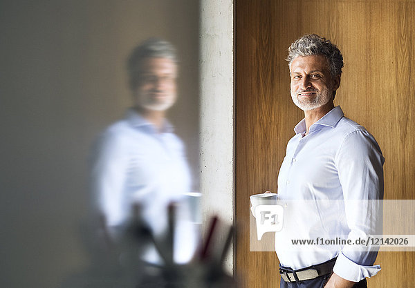 Porträt eines lächelnden reifen Geschäftsmannes mit Kaffeetasse