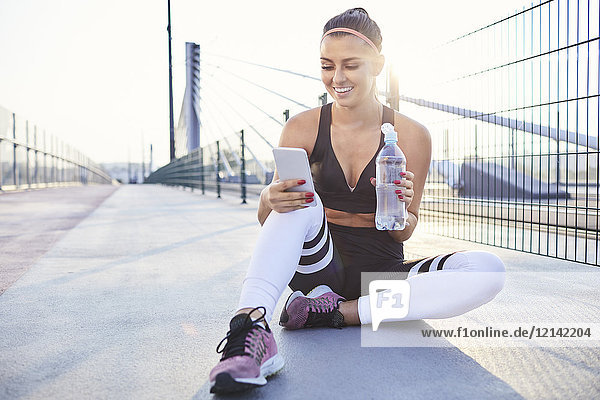 Sportlerin trinkt Wasser und überprüft ihr Handy nach dem Training