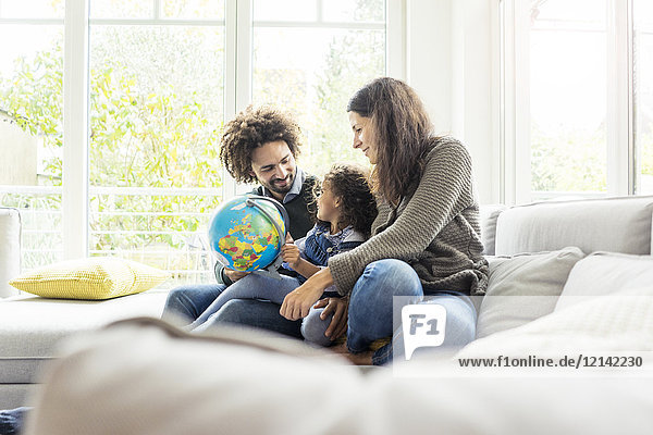 Glückliche Familie sitzend auf Couch mit Globus  Tochter lernt Geographie