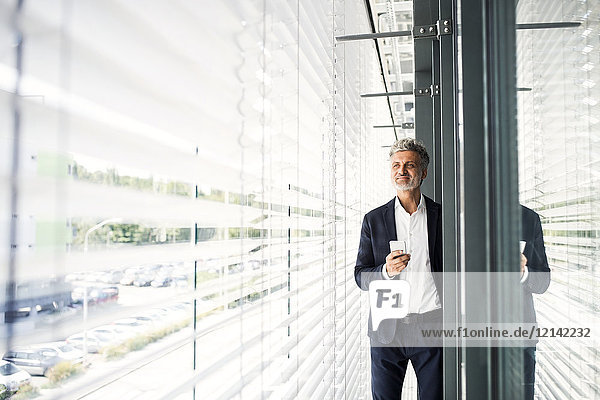 Mature businessman standing at outside sunblind holding cell phone