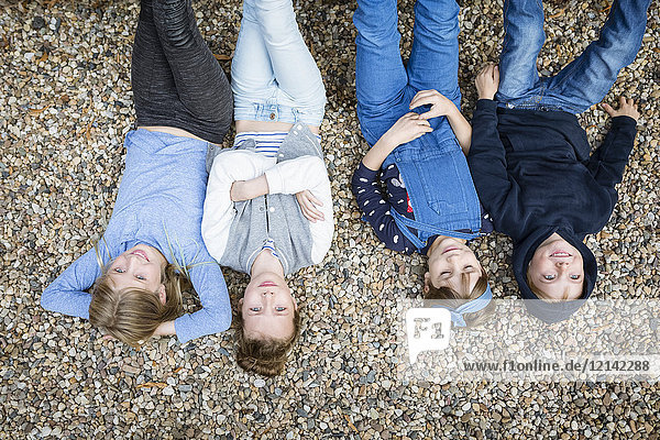 Drei Mädchen und ein Junge liegen auf dem mit Kieselsteinen bedeckten Boden.